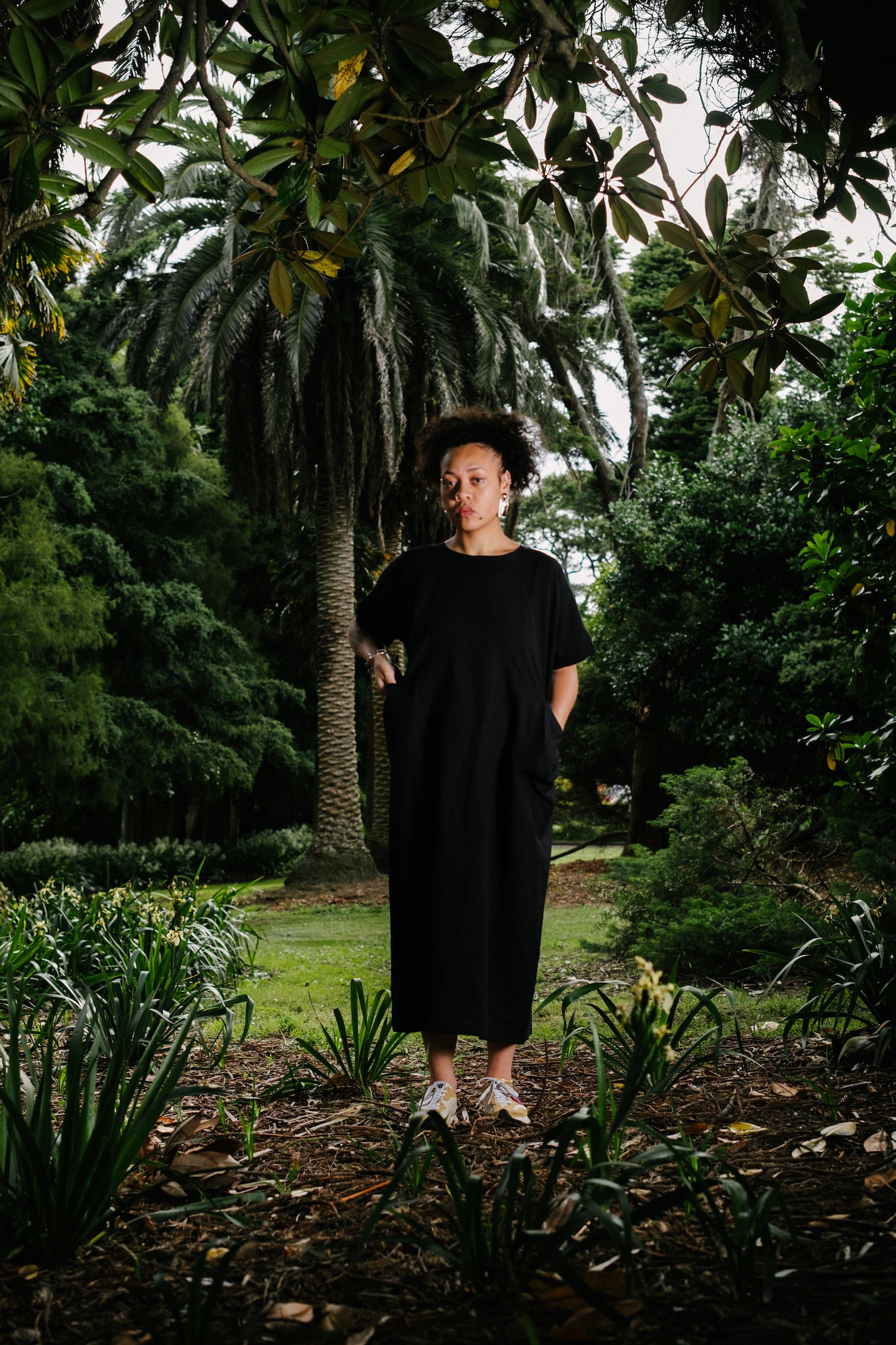 Pacific island artist, Nita wearing black short sleeve cotton seersucker long dress in front of palm tress in south Auckland