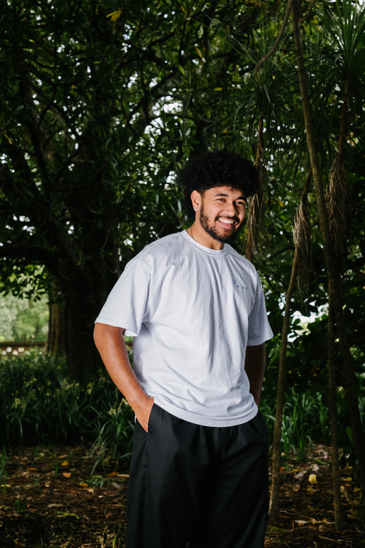 Pacific artist keciano wearing white AS colour t-shirt with Papa written on the front and Taro drawing on the back standing in the bush