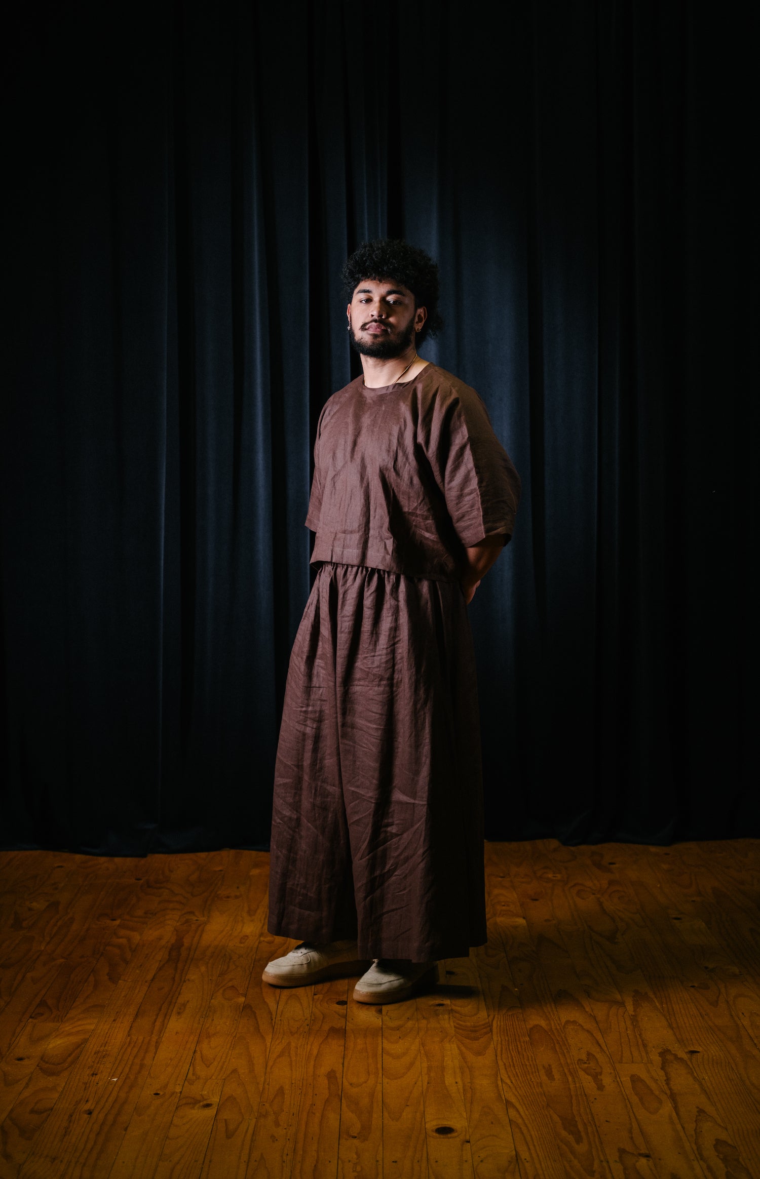 Pacific artist, Keciano wearing a brown linen crop top with matching wide leg pants in a theatre
