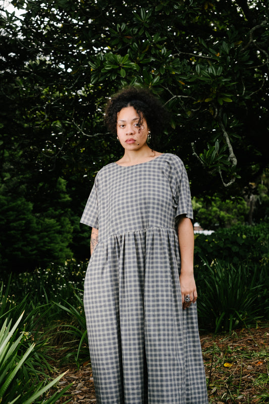 Pacific Island artist wearing grey tone check reversible dress with short sleeves and gathered waist standing amongst trees