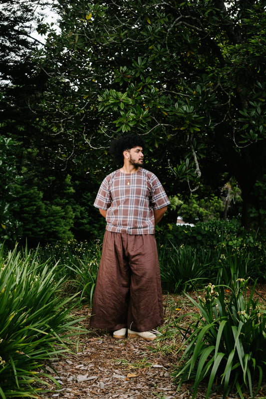 Pacific artist, Keciano wearing brown linen wide leg pants with brown plaid cotton tee in a park