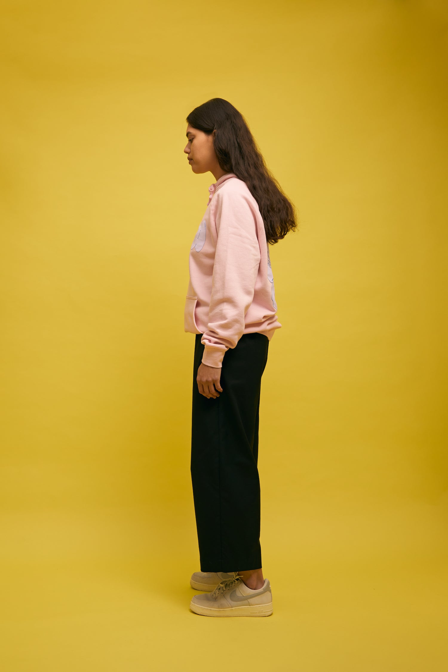 Karen Valerie standing in front of yellow wall wearing pink AS colour hoodie with Papa text on front and Hibiscus on the back