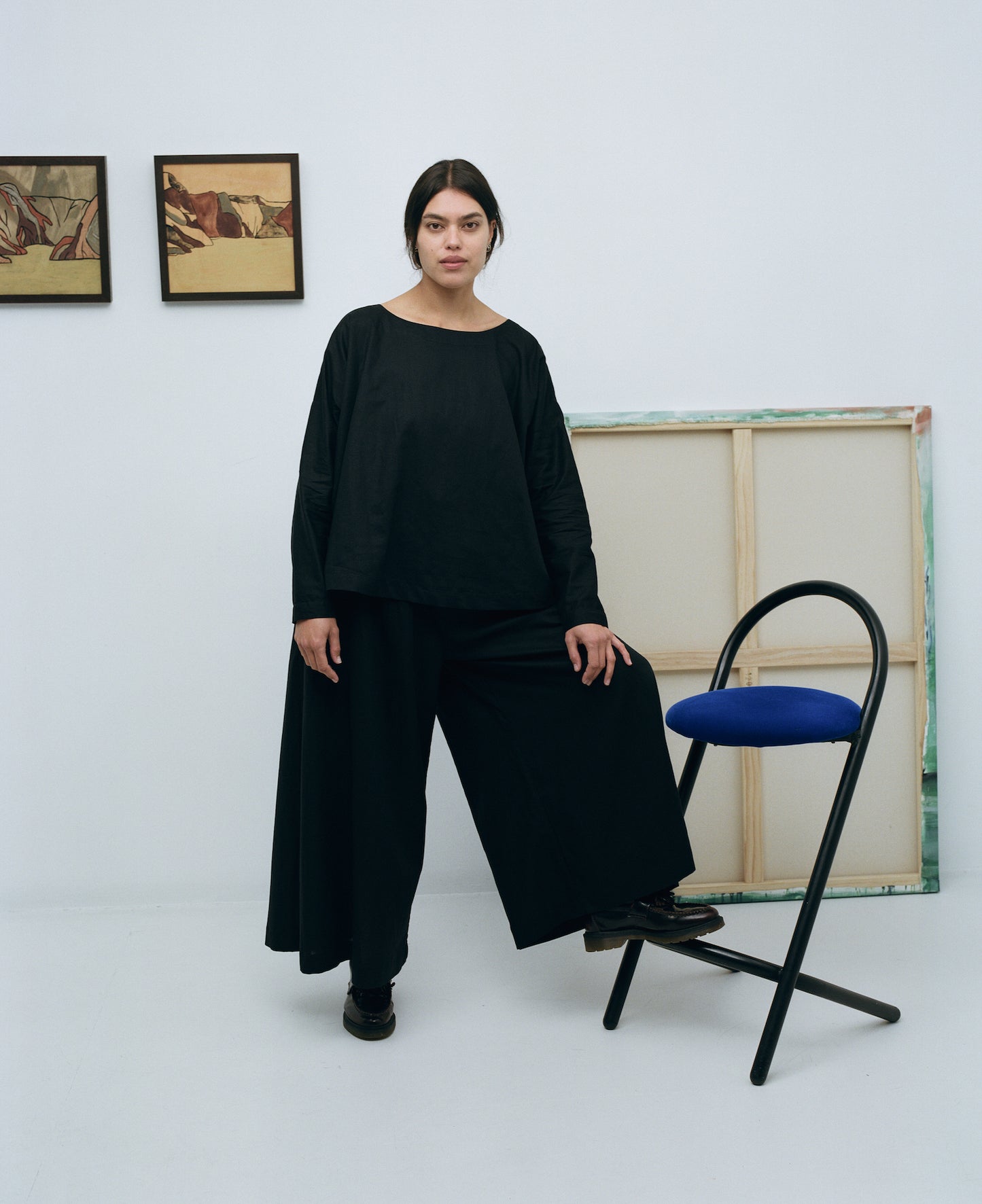 Karen wearing a black long sleeve linen cotton top with matching black linen cotton wide leg pants in an art gallery with foot on a stool