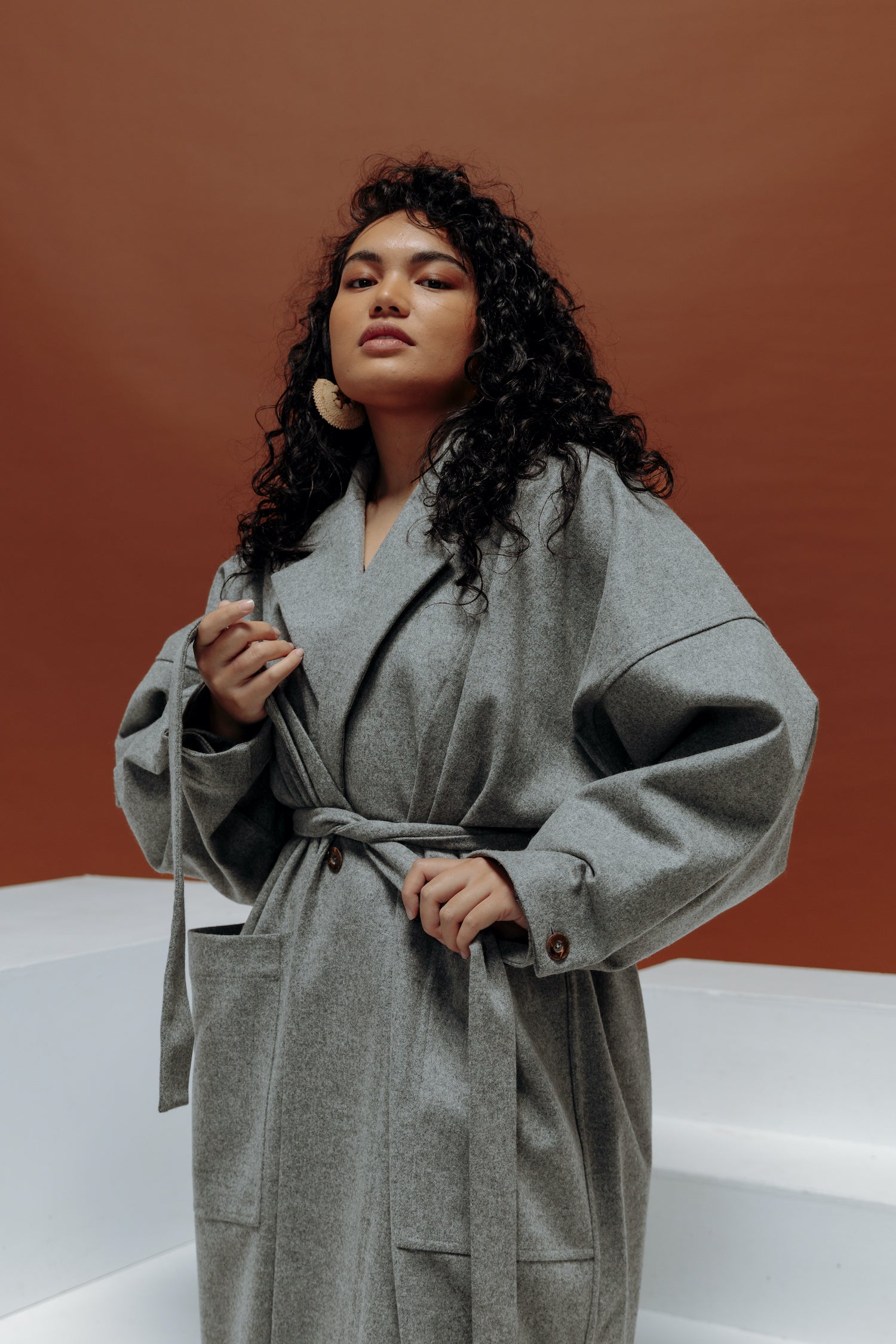 Jalaina wearing a long grey wool coat pulling the tie around her waist